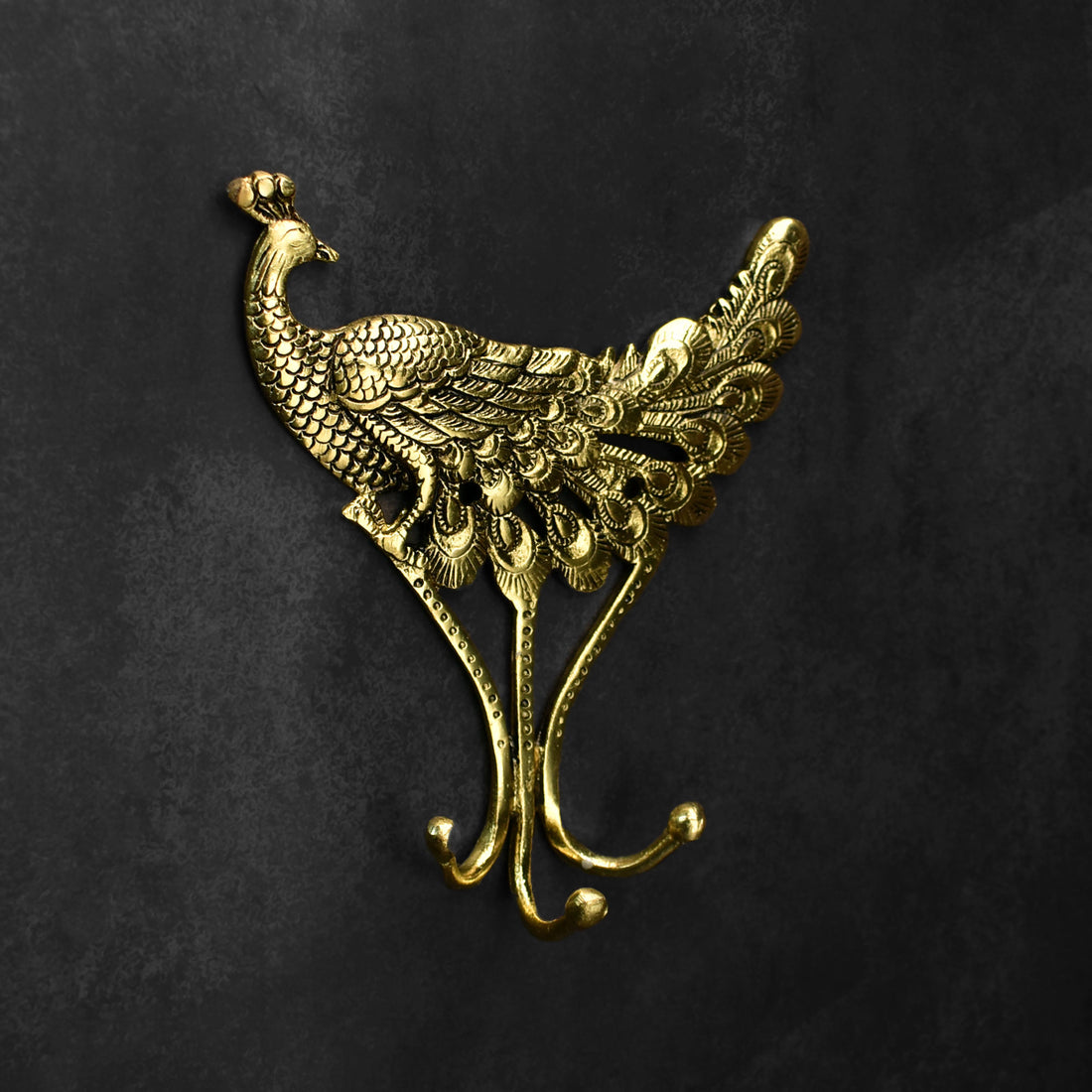 Gold peacock-shaped wall hook on a black background